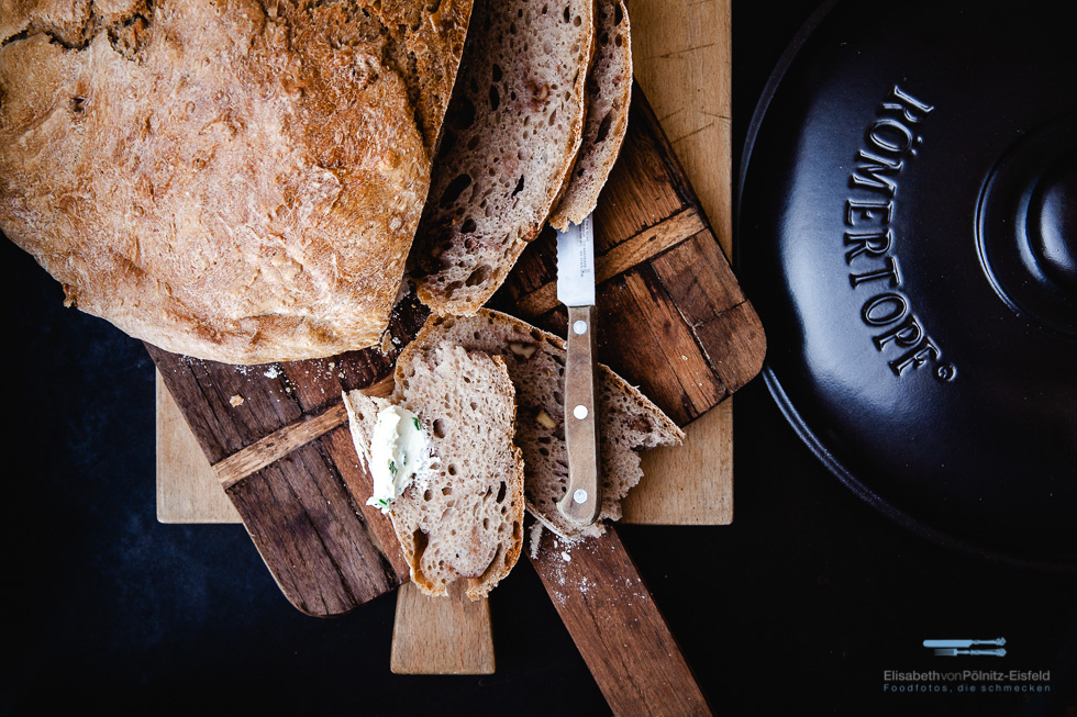 aufgeschnittenes Brot neben dem Deckel des Römertopf Schmortopfs.